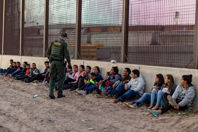 Border patrol agent lines migrants who surrendered against a wall